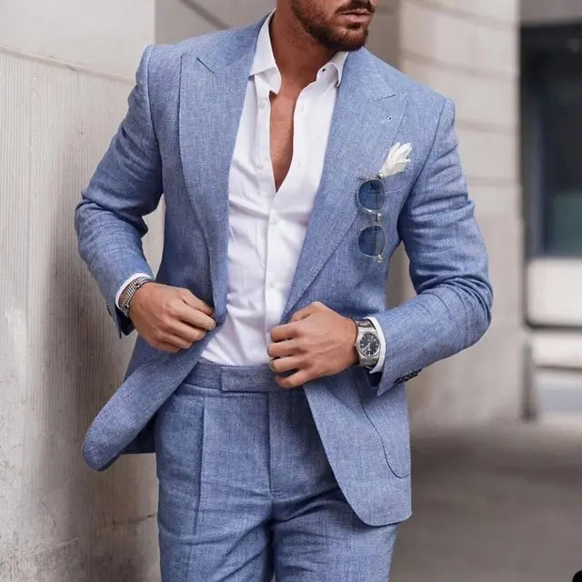 Homme en costume bleu élégant, chemise blanche ouverte, lunettes de soleil accrochées, montre-bracelet argentée, style mode urbaine chic.