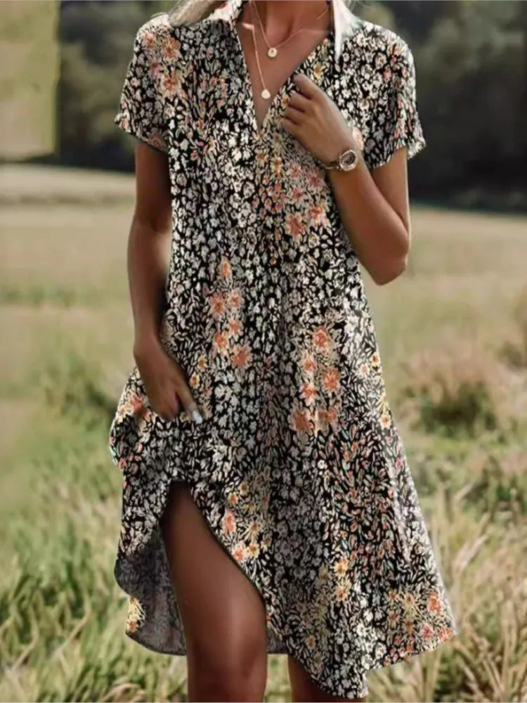 Robe d'été fleurie noire et orange, manches courtes, col en V, portée par une femme dans un champ verdoyant. Mode féminine, style décontracté.