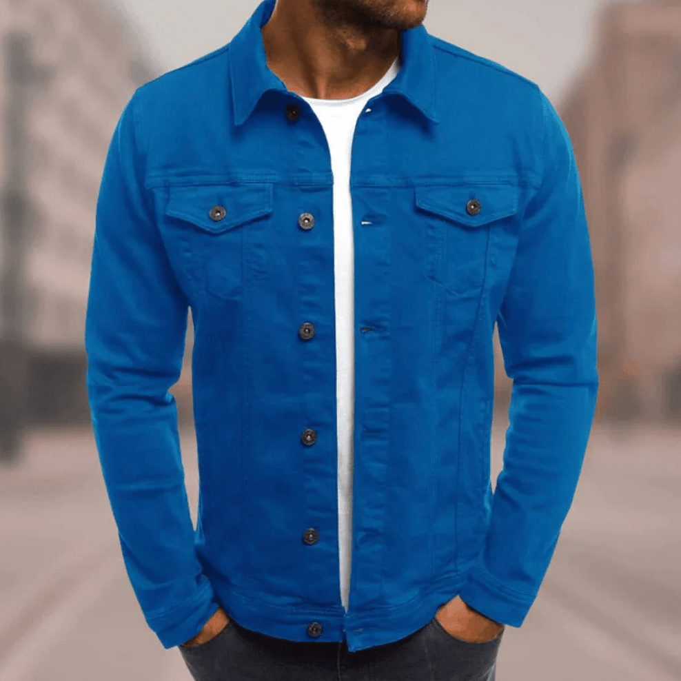 Homme portant une veste en jean bleu vif, chemise blanche en dessous, debout dans une rue floue. Mode masculine, style décontracté.