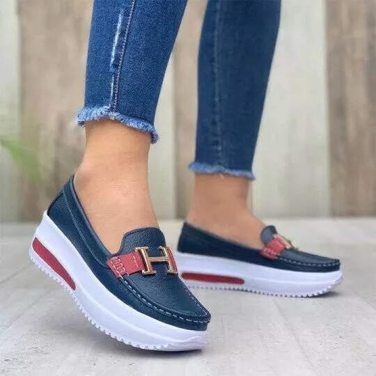 Chaussures mocassins bleu marine avec semelle plateforme blanche, détail boucle dorée et bande rouge, portées avec un jean ajusté.