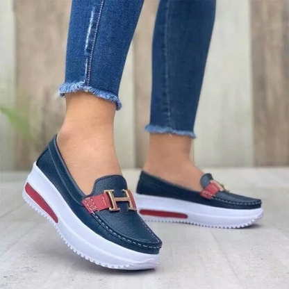 Chaussures mocassins bleu marine avec semelle plateforme blanche, détail boucle dorée et bande rouge, portées avec un jean ajusté.