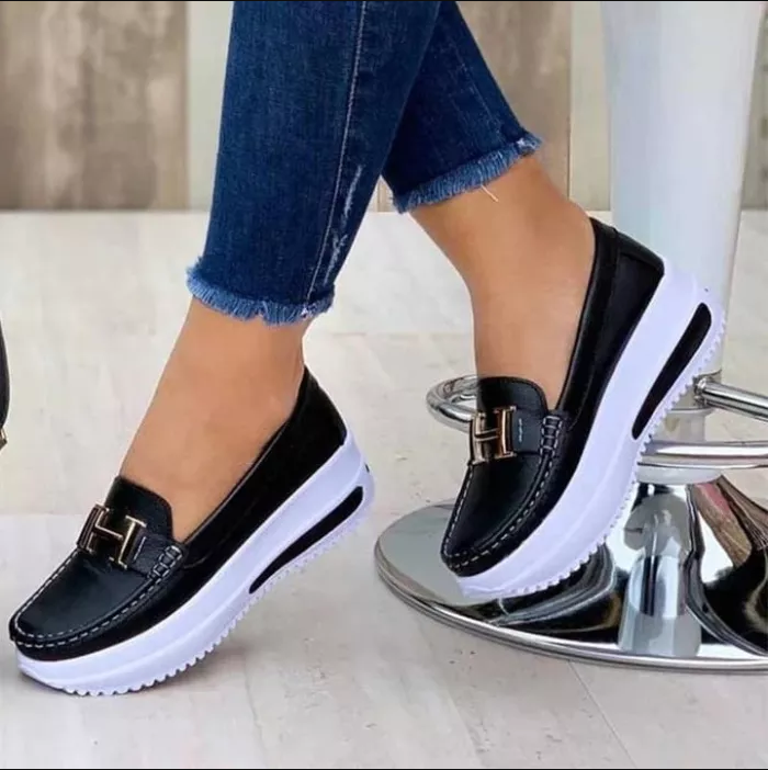 Chaussures mocassins noirs pour femmes avec semelles compensées blanches, portées avec un jean bleu. Mode féminine, chaussures confortables et élégantes.