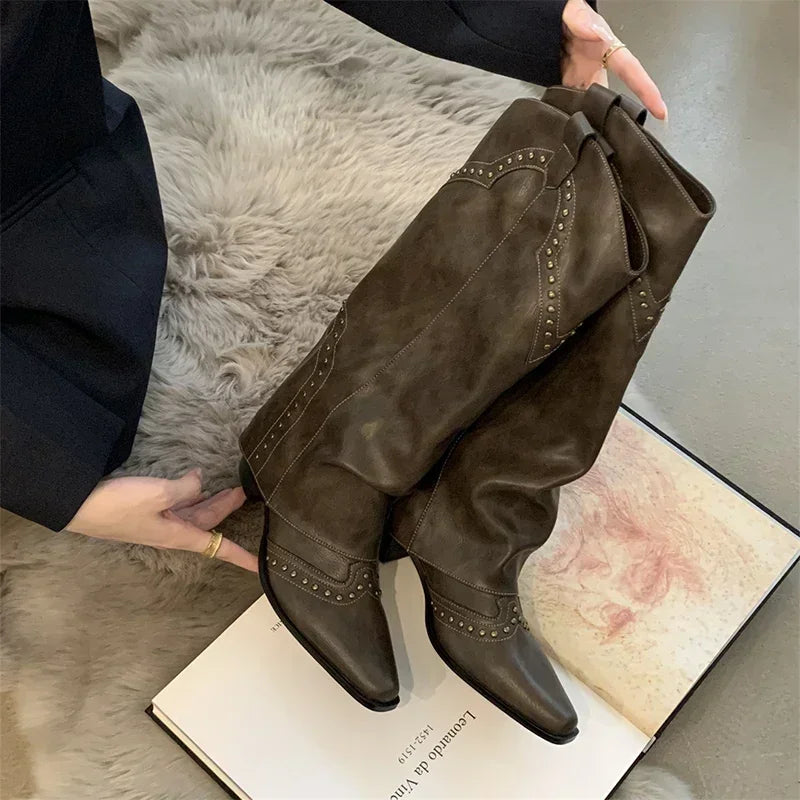 Brune cowboystøvler med nitter på en åben bog og pelsunderlag. Trendy fodtøj, westernstil, mode til kvinder, stilfulde støvler.