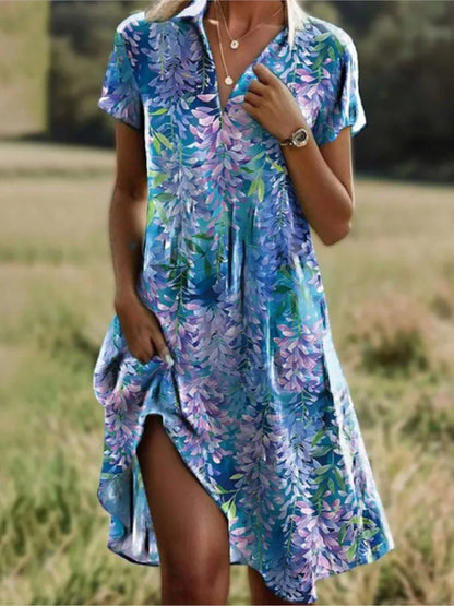 Robe d'été fleurie bleue et violette, manches courtes, col en V, portée par une femme dans un champ. Mode féminine, style décontracté.