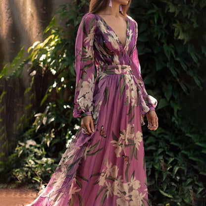 Robe longue fleurie rose avec manches longues, motif floral tropical, portée dans un jardin verdoyant. Mode élégante, style bohème chic.