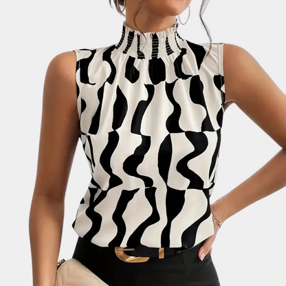 Femme portant un haut sans manches à motifs noir et blanc, col montant plissé, tenant un sac beige. Mode élégante et moderne.