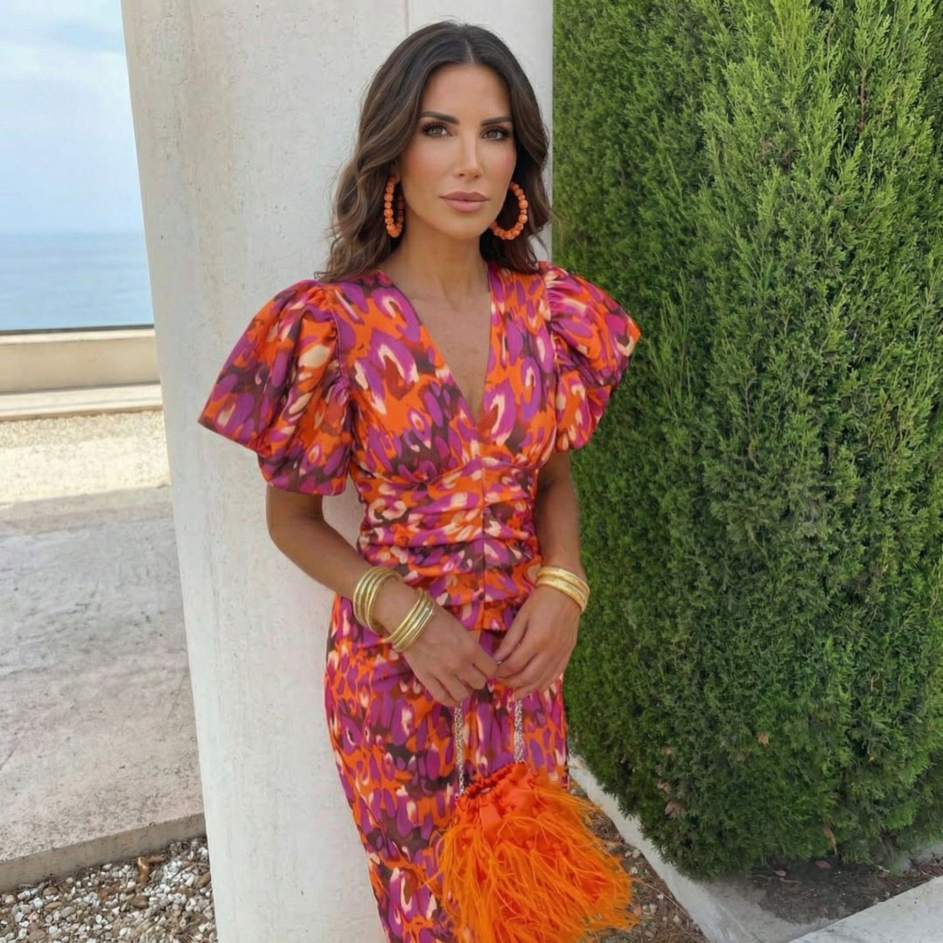 Woman in a colorful dress standing next to a column with greenery in the background