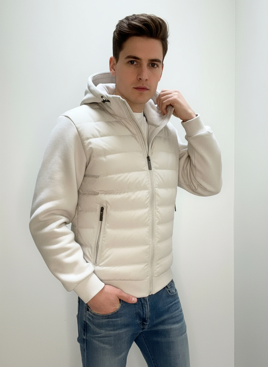 Ung mand iført hvid hættejakke og blå jeans, poserer i minimalistisk rum. Moderne herremode, vinterjakke, casual stil.