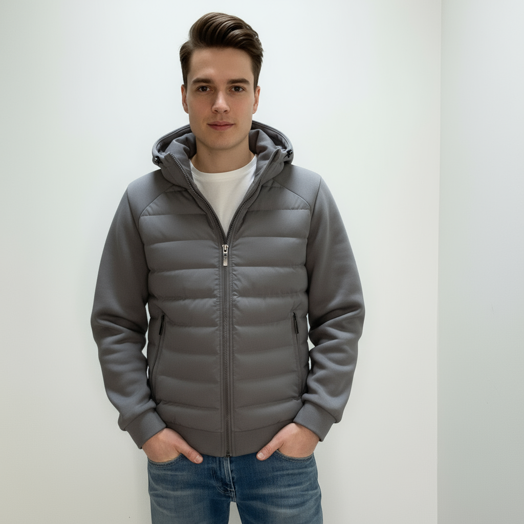 Ung mand iført grå hættejakke og jeans, står mod hvid baggrund. Moderne herremode, vinterjakke, casual stil, komfortabelt tøj.