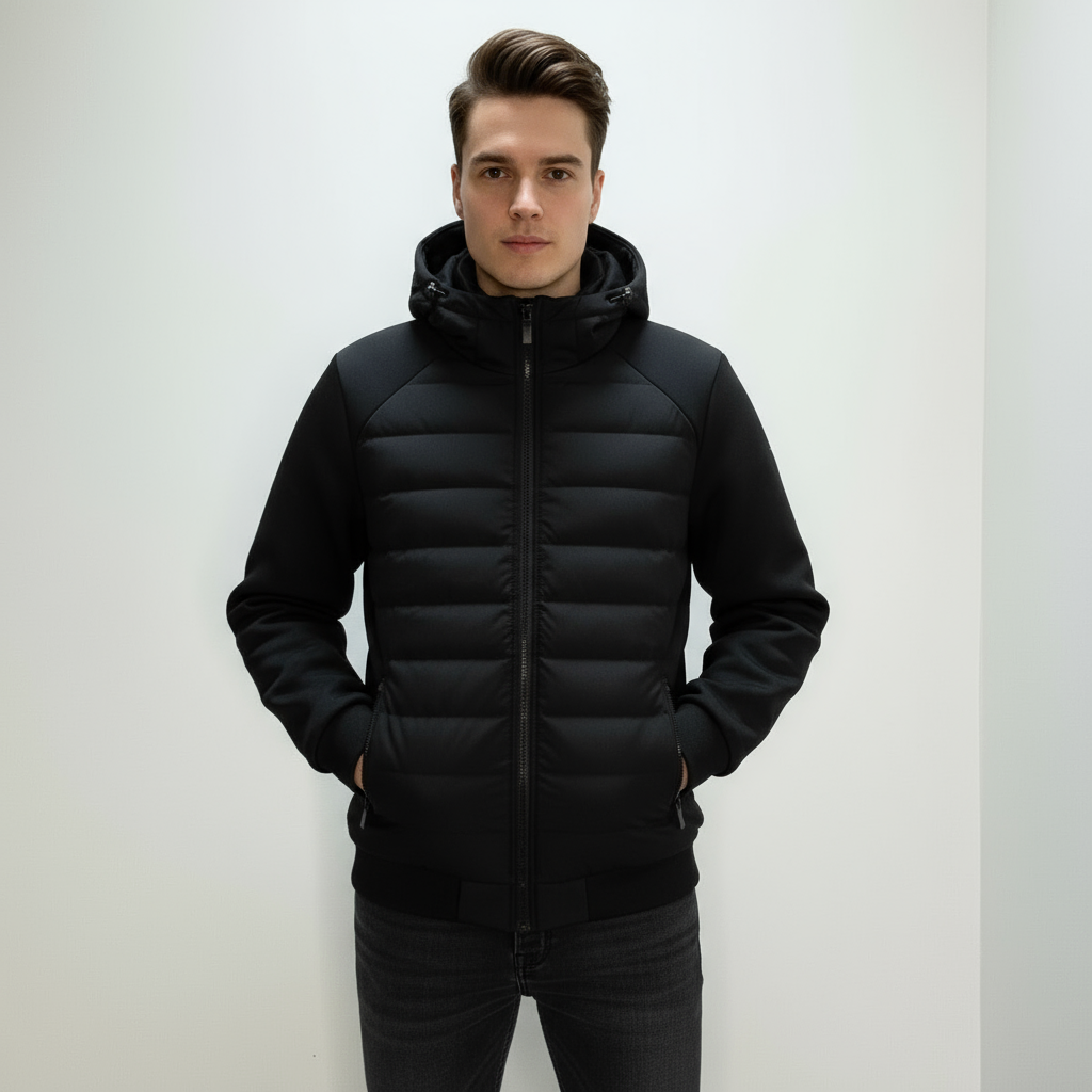 Ung mand iført sort, polstret jakke med hætte, står mod hvid baggrund. Vintermode, herrejakke, stilfuldt overtøj, moderne design.