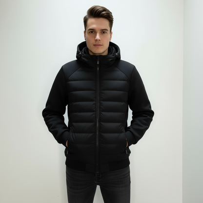Ung mand iført sort, polstret jakke med hætte, står mod hvid baggrund. Vintermode, herrejakke, stilfuldt overtøj, moderne design.