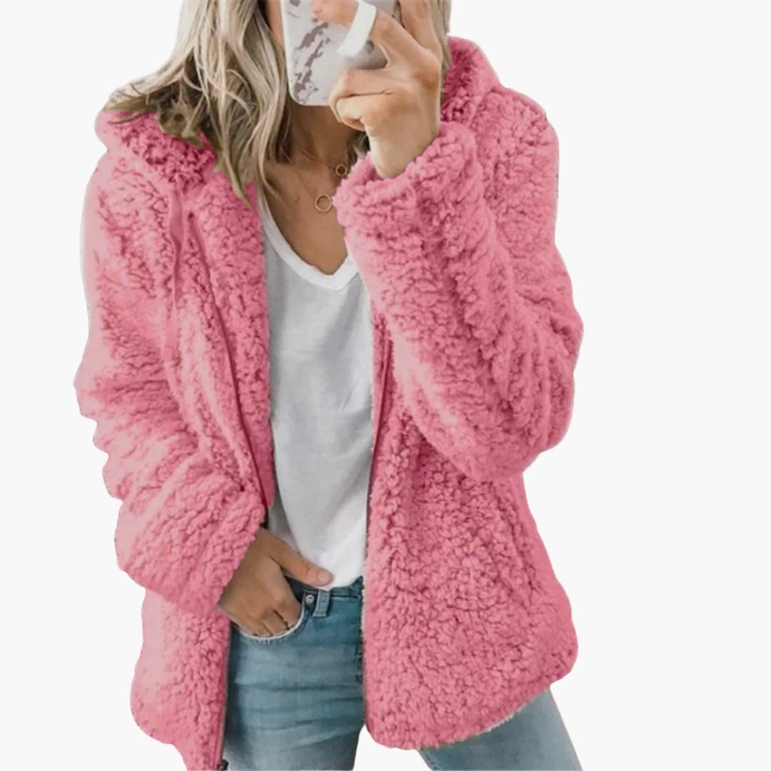 Femme portant une veste en fausse fourrure rose, tenue décontractée avec jean bleu et t-shirt blanc, style mode automne-hiver tendance.