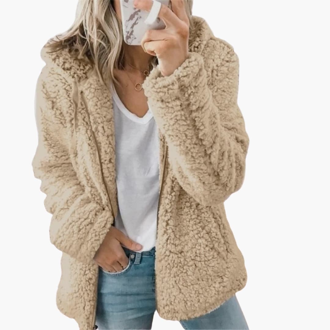 Femme portant une veste en fausse fourrure beige, tenant un smartphone. Mode automne-hiver, look décontracté, tendance vestimentaire féminine.