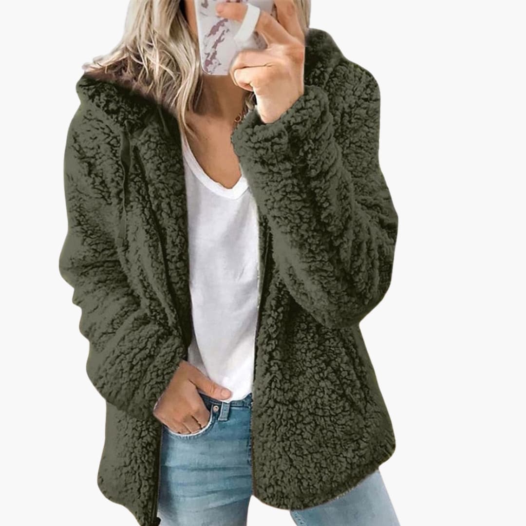 Femme portant une veste en fausse fourrure verte, tenue décontractée avec jean bleu et t-shirt blanc, mode automne-hiver tendance.