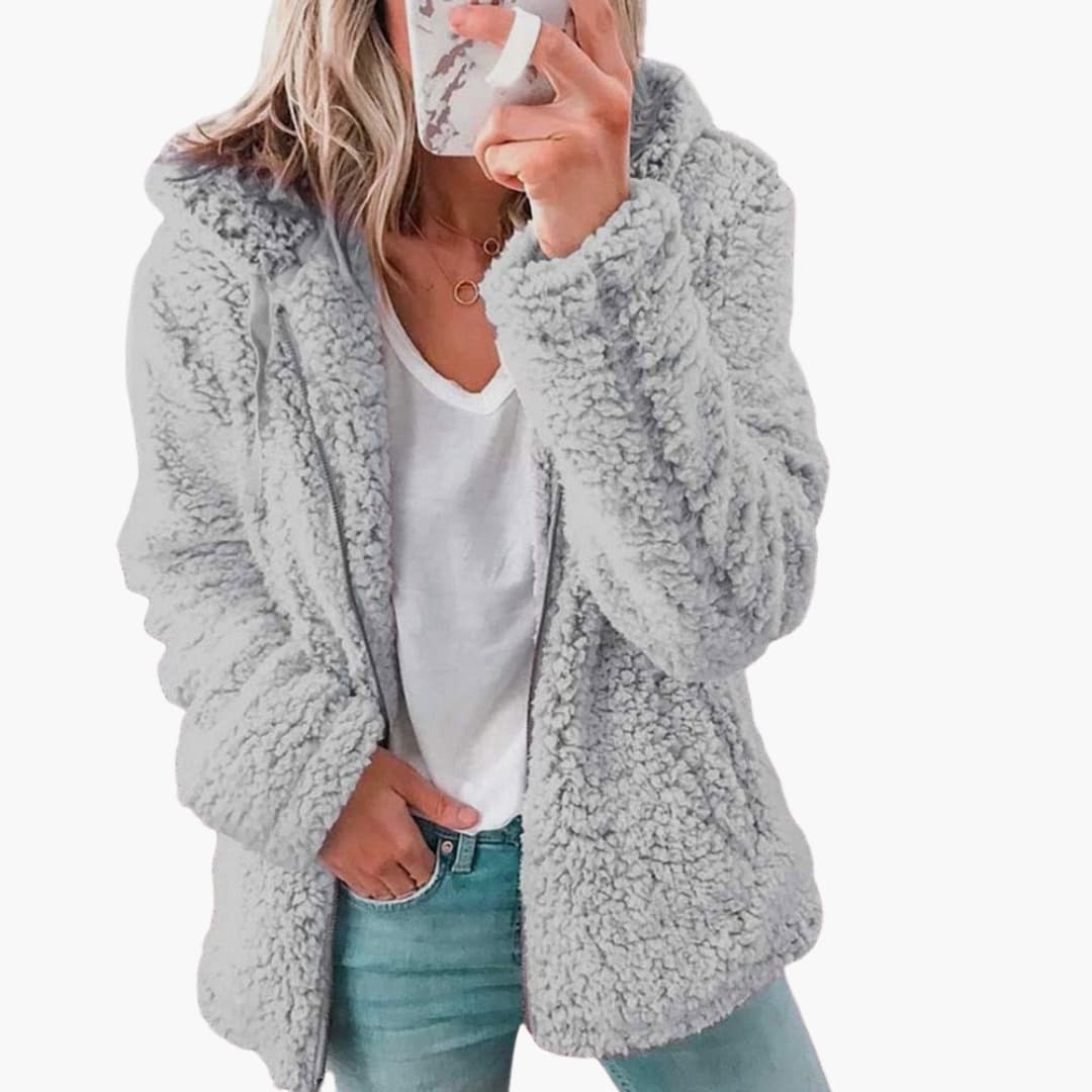 Femme portant une veste en fausse fourrure grise, tenant un smartphone. Mode hiver, style décontracté, tendance vestimentaire féminine.