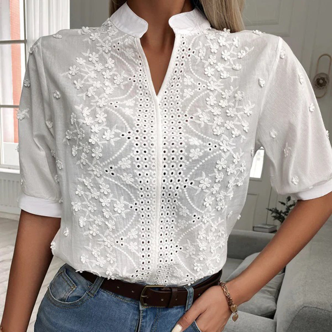Frau in weißer, bestickter Bluse mit Blumenmuster, Stehkragen und halblangen Ärmeln.