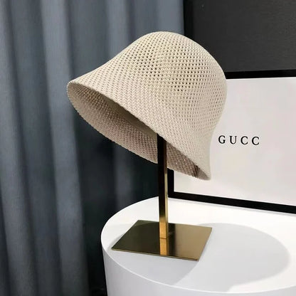Chapeau cloche en tricot beige sur support doré, devant une boîte Gucci. Accessoire de mode élégant et tendance, idéal pour l'été.