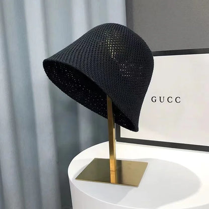 Chapeau cloche noir en maille sur support doré, devant une boîte Gucci. Accessoire de mode élégant et tendance, idéal pour un look chic.