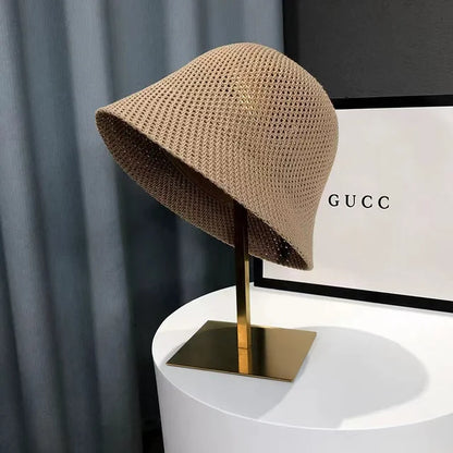 Chapeau cloche en maille beige sur support doré, devant une boîte Gucci. Accessoire de mode élégant et tendance.