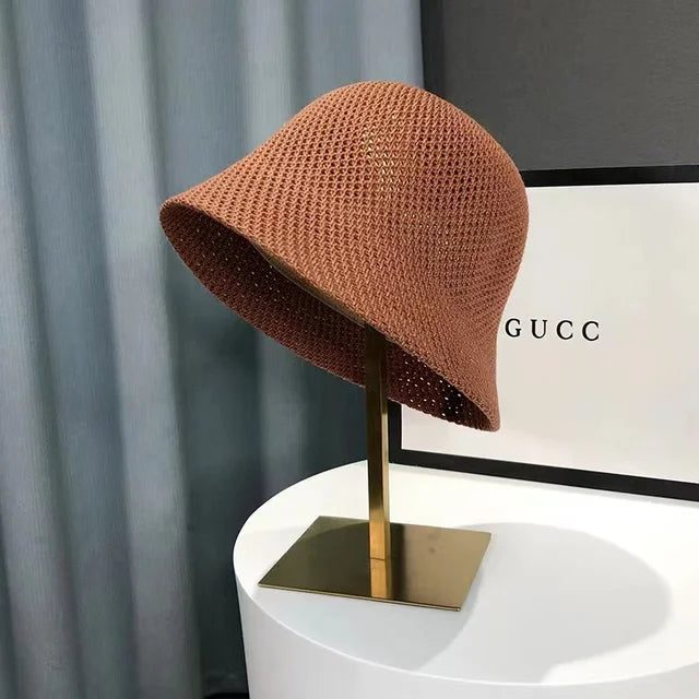 Chapeau cloche en crochet marron sur support doré, devant une boîte Gucci. Accessoire de mode élégant et tendance.
