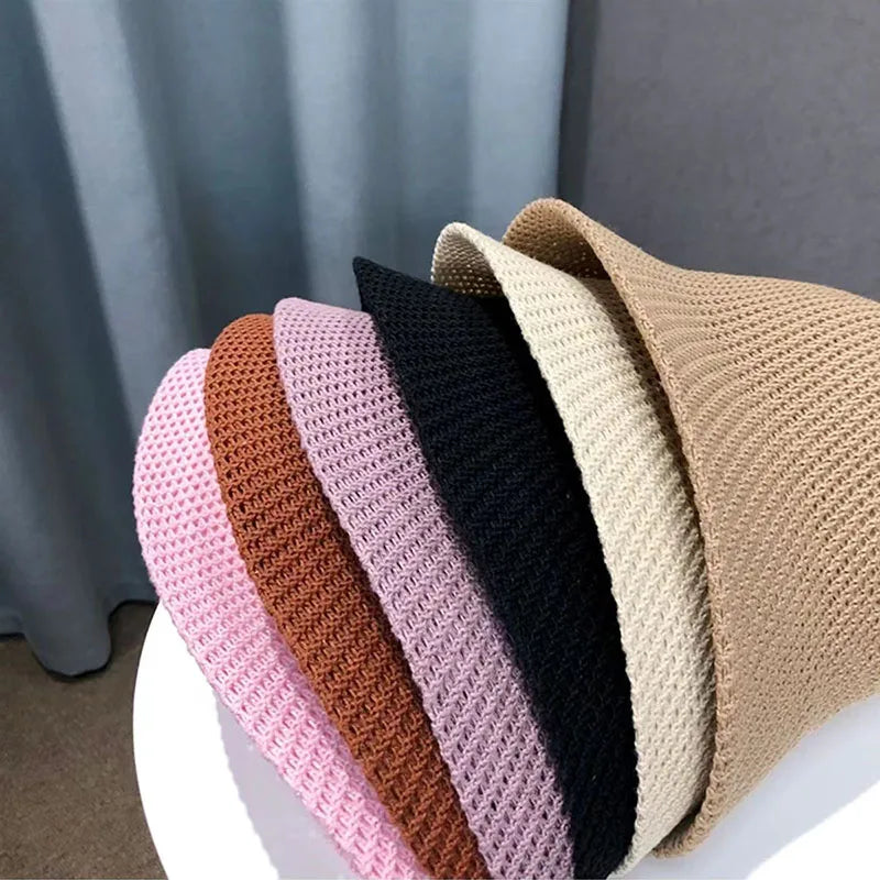 Chapeaux en paille colorés empilés sur une table blanche, incluant beige, noir, rose et marron. Accessoires de mode été, style décontracté.