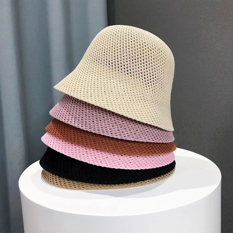 Chapeaux bob en maille empilés, couleurs beige, rose, marron et noir, sur fond gris. Accessoires mode tendance, style décontracté et moderne.