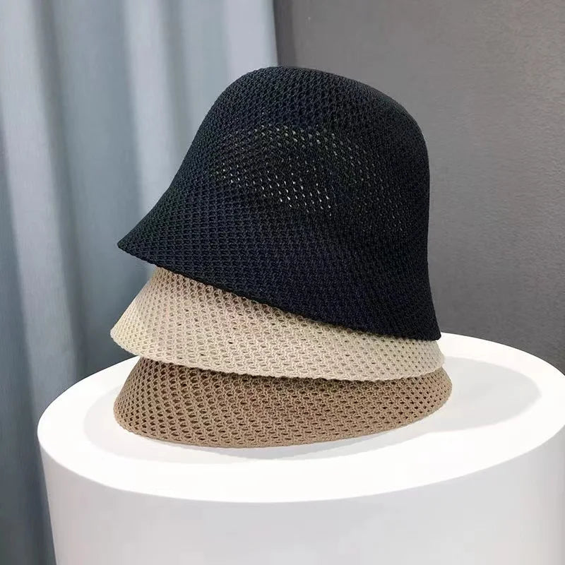 Trois chapeaux bob en maille superposés, couleurs noir, beige et marron, posés sur une table blanche. Accessoire mode tendance et élégant.