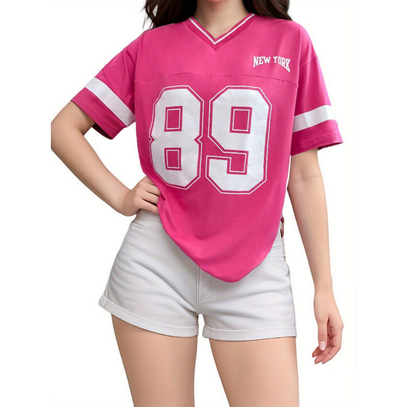 Femme portant un t-shirt rose avec le numéro 89 et l'inscription "New York", associé à un short blanc. Mode décontractée, style sportif.