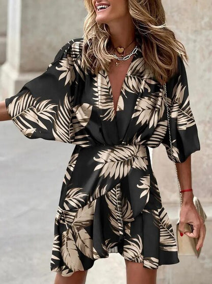 Robe noire à motifs feuillage beige, manches larges, col en V, portée par une femme souriante. Mode féminine élégante, tendance estivale.