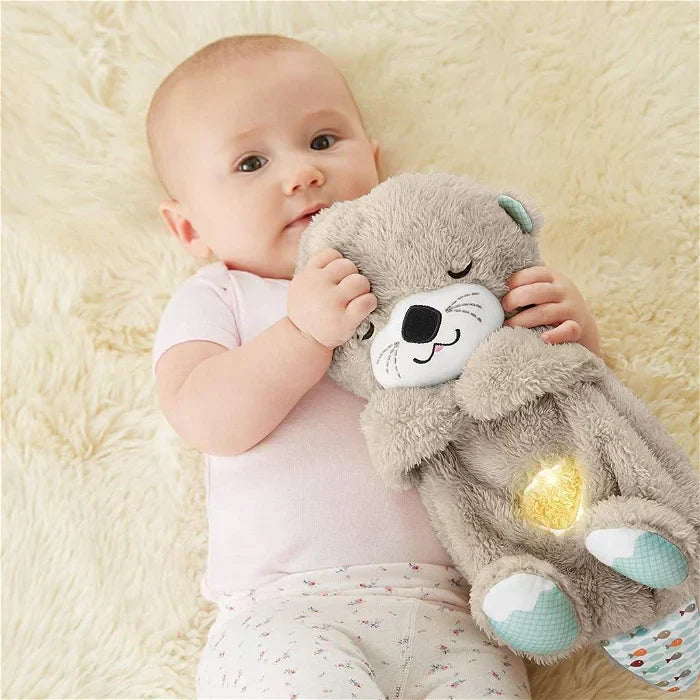 Baby mit Fisher-Price Plüschotter, grau, leuchtend, Musikspielzeug, auf Teppich liegend.