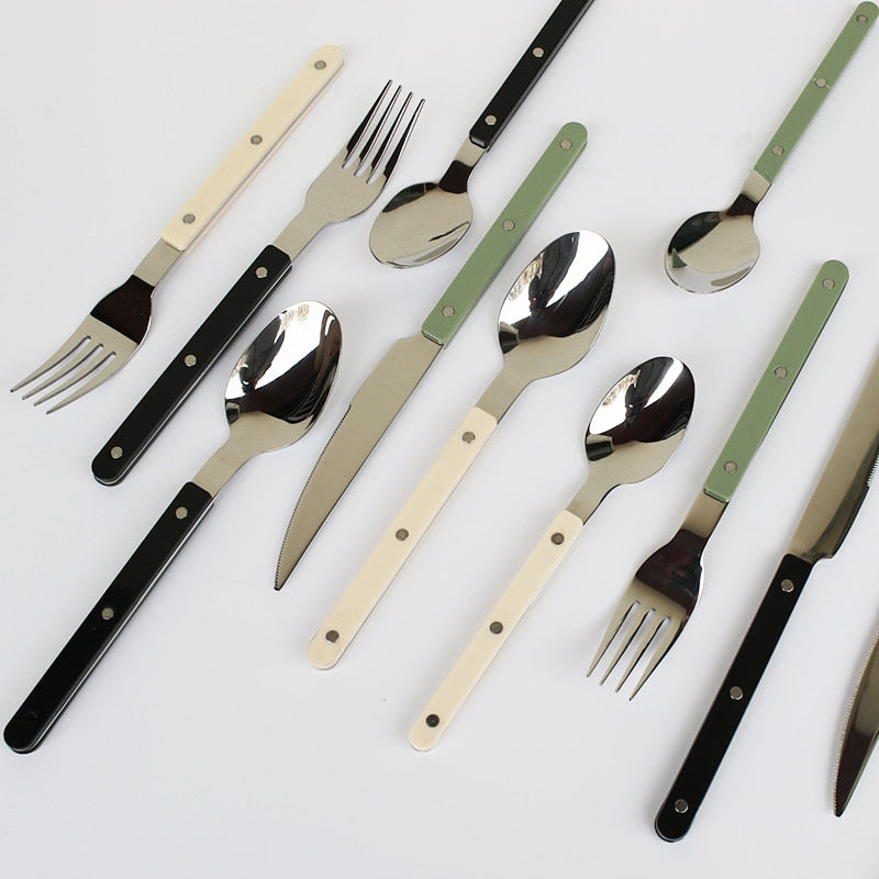 Moderne bestik med farvede håndtag i sort, hvid og grøn. Sæt inkluderer knive, gafler og skeer. Stilfuldt design til køkken og borddækning.