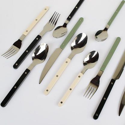 Moderne bestik med farvede håndtag i sort, hvid og grøn. Sæt inkluderer knive, gafler og skeer. Stilfuldt design til køkken og borddækning.