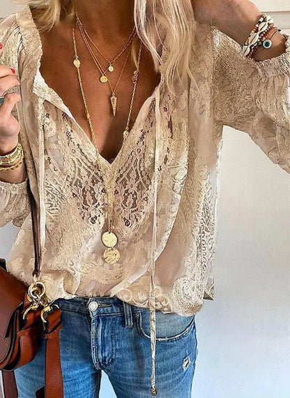 Femme portant un chemisier en dentelle beige avec col en V, colliers dorés superposés, jean bleu et sac en cuir marron. Mode élégante et décontractée.