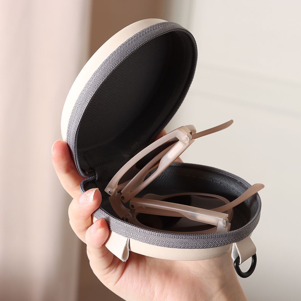 Geöffnete Brillenetui aus Stoff, beige und grau, mit Brille, handgehalten.