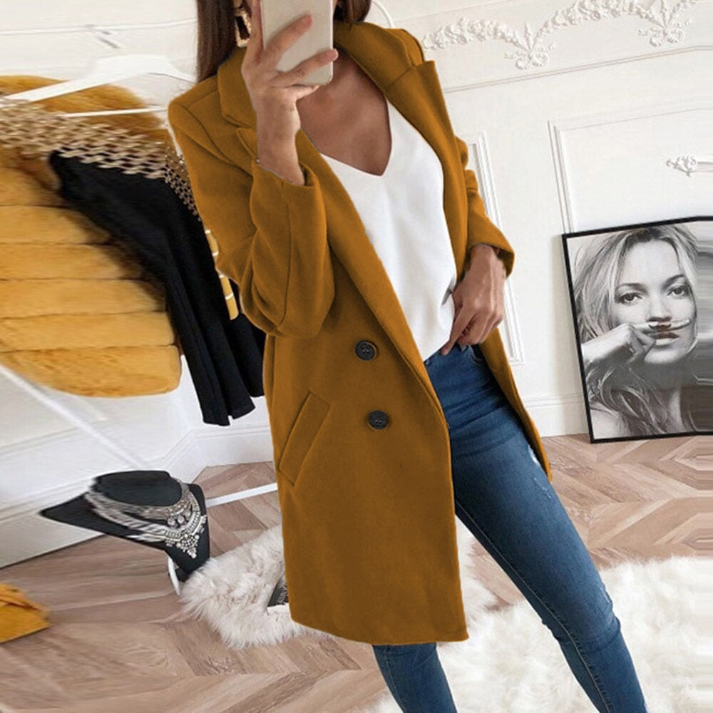 Frau im senfgelben Mantel, weiße Bluse, blaue Jeans, modernes Wohnzimmer, stilvolle Mode.