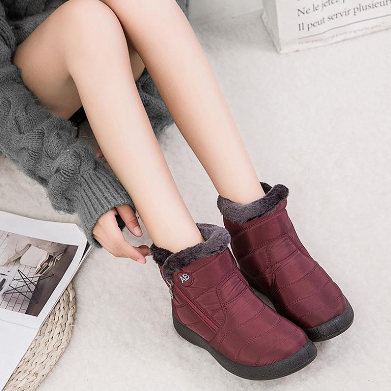 Femme portant des bottes d'hiver bordeaux avec doublure en fourrure, assise sur un tapis blanc, lisant un magazine. Mode hiver, chaussures chaudes.