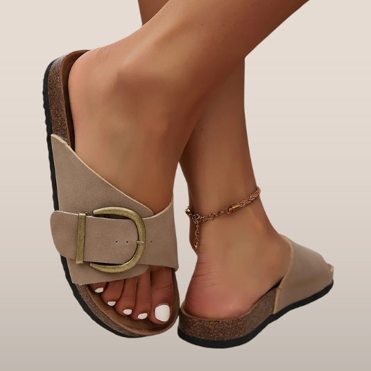 Sandales beiges à semelle en liège, boucle dorée, portées avec une chaîne de cheville dorée. Mode estivale, chaussures confortables pour femmes.