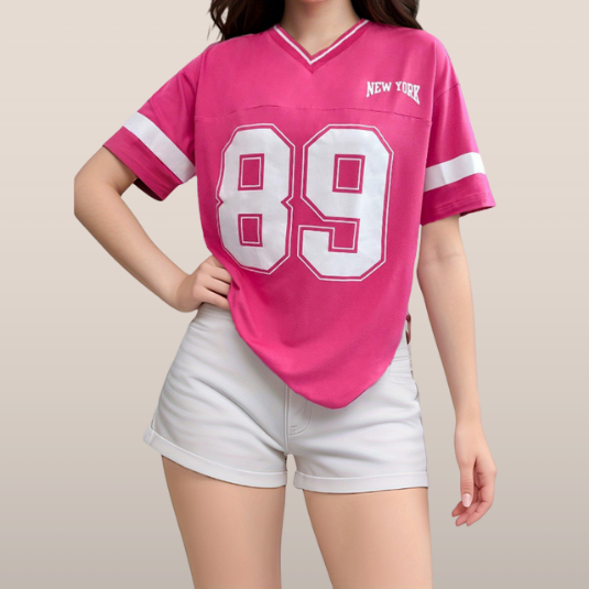 Femme portant un t-shirt rose avec numéro 89 et inscription "New York", associée à un short blanc. Mode décontractée, style sportif tendance.