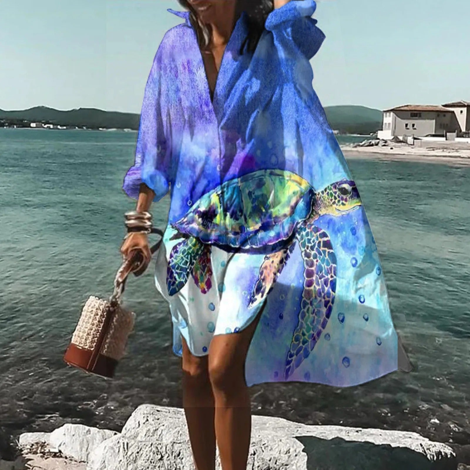 Femme en robe de plage bleue avec motif tortue, bord de mer en arrière-plan, sac à main en osier. Mode estivale, tenue décontractée bord de mer.