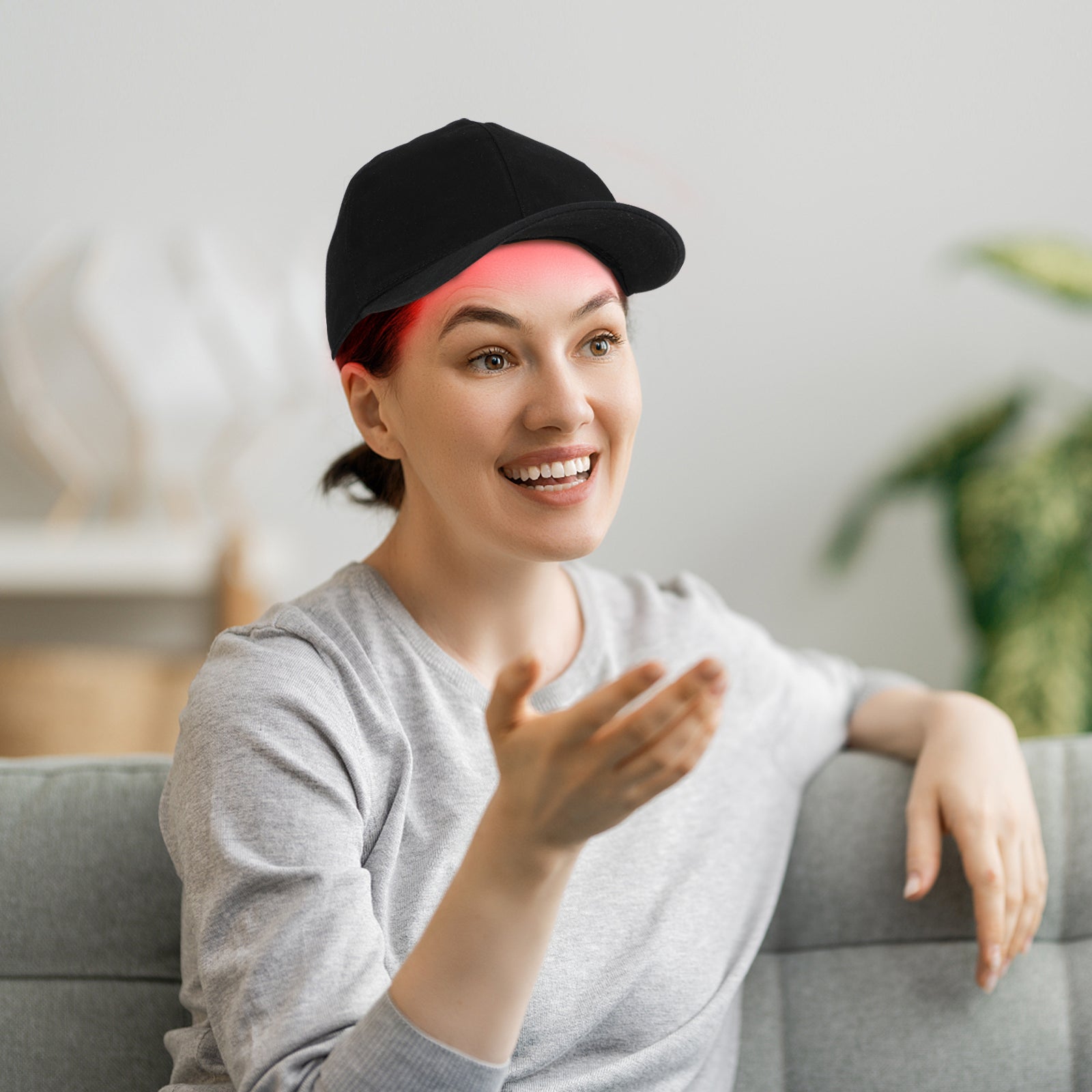 Frau mit schwarzer Baseballkappe und grauem Pullover lächelt auf Sofa, moderne Wohnzimmereinrichtung.