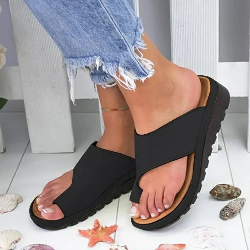 Kvinde iført sorte sandaler med ergonomisk sål, kombineret med lyseblå jeans. Perfekt til sommermode og komfortabelt fodtøj.