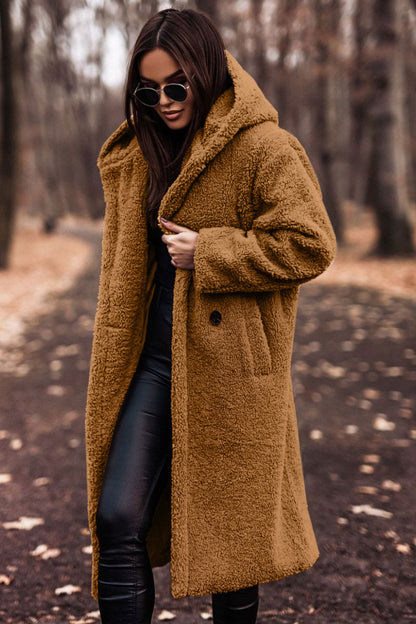 Femme portant un manteau en fausse fourrure marron, lunettes de soleil, pantalon noir, marchant dans un parc automnal. Mode hiver, style urbain.