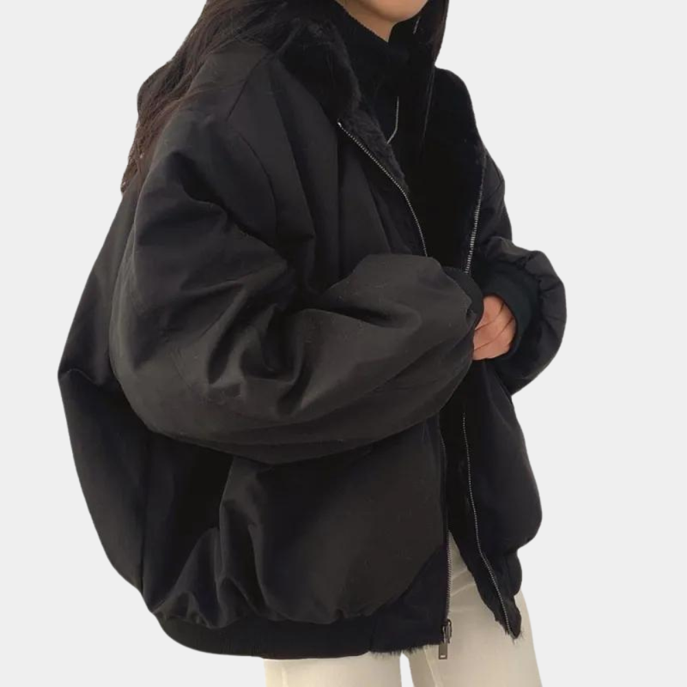 Sort oversized jakke til kvinder, med lynlås og hætte, bæres over sort trøje og hvide bukser. Trendy vintermode, komfortabel og stilfuld.