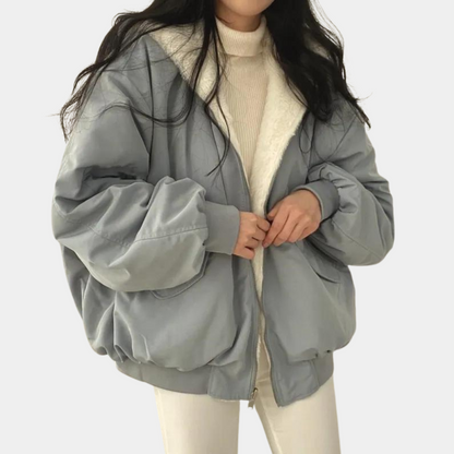 Kvinde iført lyseblå oversized jakke med hvid pelsfor, beige sweater og hvide bukser. Trendy vintermode, casual stil, komfortabelt tøj.