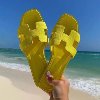 Gelbe Sandalen am Strand, Sommermode, Damen Flip-Flops, Strandurlaub, sonniger Tag, Meereshintergrund.