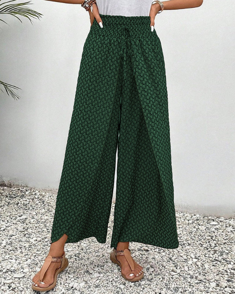 Pantalon large vert à motifs géométriques, porté par une femme sur fond de gravier. Mode estivale, style décontracté, tendance féminine.