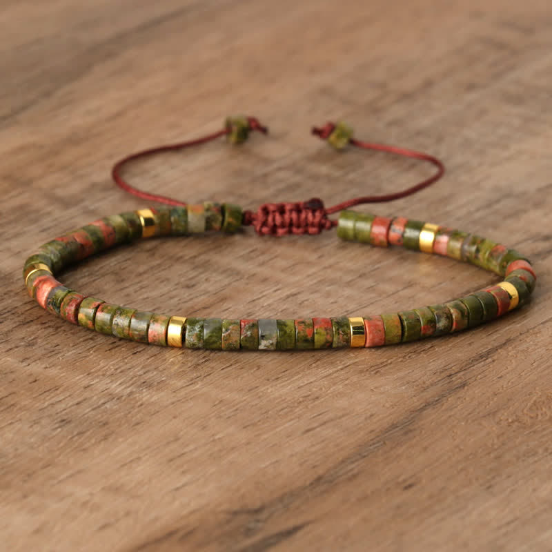 Grünes Steinarmband mit roten Akzenten, verstellbar, handgefertigt, auf Holztisch.