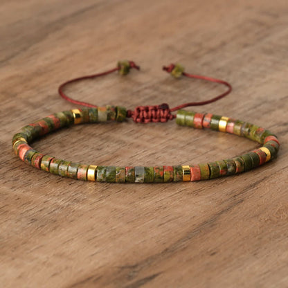 Grünes Steinarmband mit roten Akzenten, verstellbar, handgefertigt, auf Holztisch.