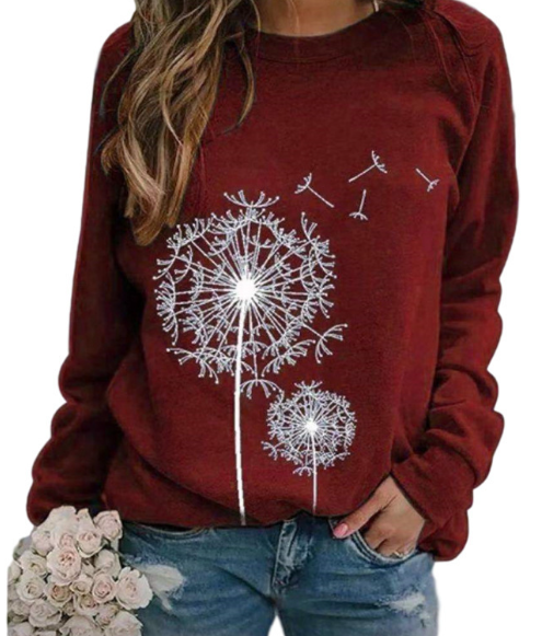 Femme portant un pull rouge avec motif de pissenlits blancs, tenant un bouquet de roses blanches. Mode décontractée, tendance automne.