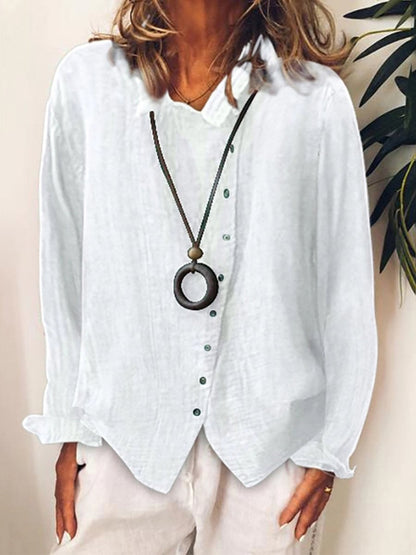 Chemisier blanc en lin pour femme avec col en V, manches longues et boutons verts, accompagné d'un collier pendentif circulaire. Mode élégante et décontractée.